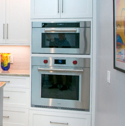 This is a picture of a bright and open kitchen in Nokomis, Florida with custom made cabinetry by Kountry Kraft Cabinetry- featuring the custom made drop-down oven and microwave from Wolf. 