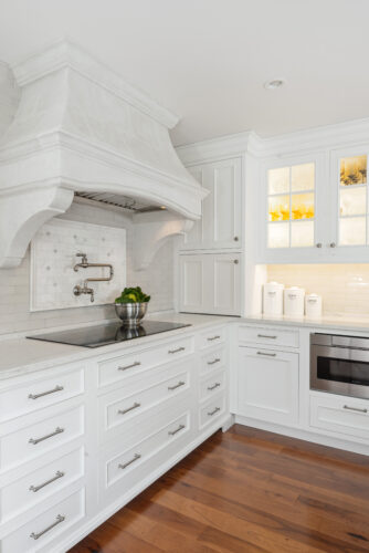 This is a picture of the stovetop and double oven in a white kitchen with custom cabinets by Kountry Kraft Cabinetry.