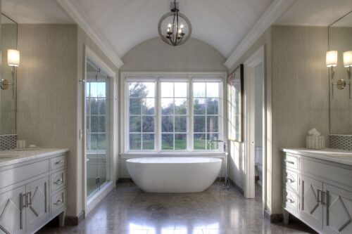 This is a picture of an open and white bathroom with a luxurious white stand-alone bath in the center, with custom cabinetry made by Kountry Kraft Cabinetry. 