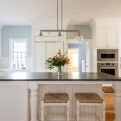 A white kitchen with pale blue walls, a kitchen island with seating and wolf wall ovens