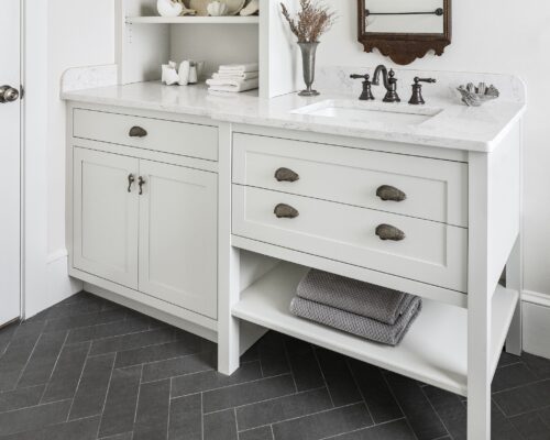 Detail of vanity cabinetry in a bathroom remodel in Exeter NH with seashell drawer pulls, seahorse door pulls, and marble countertop.
