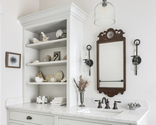 Bathroom remodel in Exeter NH with custom maple cabinetry, antique wood mirror, black sconces, and white marble countertop.