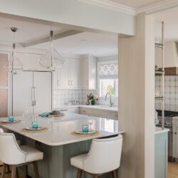 Seaside kitchen in Massachusetts with custom cabinets in Balboa Mist and Greyhound, marble countertops, and pendant lighting.