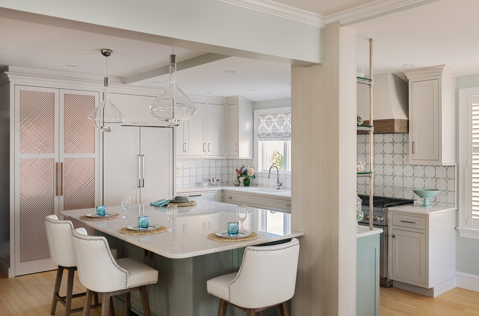 Seaside kitchen in Massachusetts with custom cabinets in Balboa Mist and Greyhound, marble countertops, and pendant lighting.