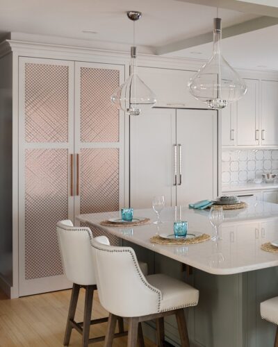 Pantry with rose-gold mesh doors beside integrated refrigerator in a Massachusetts kitchen with custom cabinetry.
