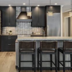 Modern kitchen with custom kitchen cabinets in Exeter NH featuring black cabinetry, stainless steel island, and wood flooring.