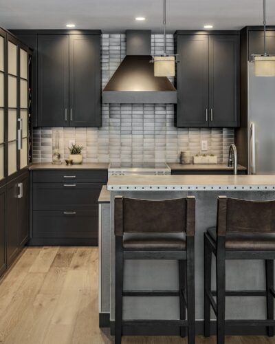 Portrait view of custom kitchen cabinets Exeter NH featuring black perimeter cabinetry and hammered stainless steel island.