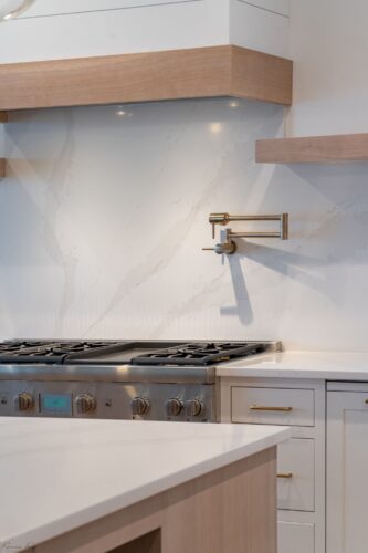 Close-up of Thermador 6-burner range with quartz backsplash, brass pot filler, and custom maple cabinetry in Avalon NJ coastal kitchen.