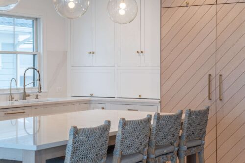 Island seating in Avalon NJ coastal kitchen with custom cabinets, quartz countertops, brass fixtures, and chevron wood-paneled appliances.