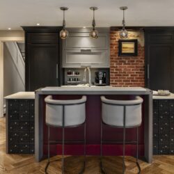 Full view of custom kitchen cabinets in Exeter NH featuring a brick accent wall, central island with seating, and layered lighting design.
