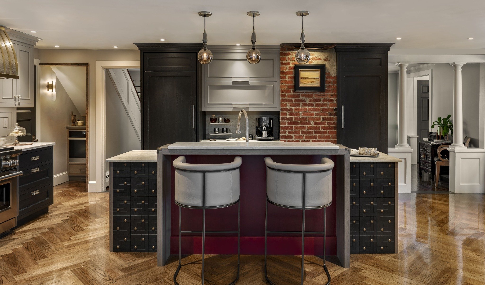 Full view of custom kitchen cabinets in Exeter NH featuring a brick accent wall, central island with seating, and layered lighting design.