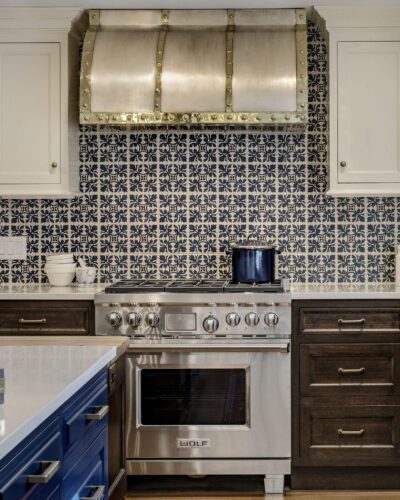 Wolf range framed by custom kitchen cabinets in Exeter NH with a bold patterned backsplash and custom metal hood with brass accents.