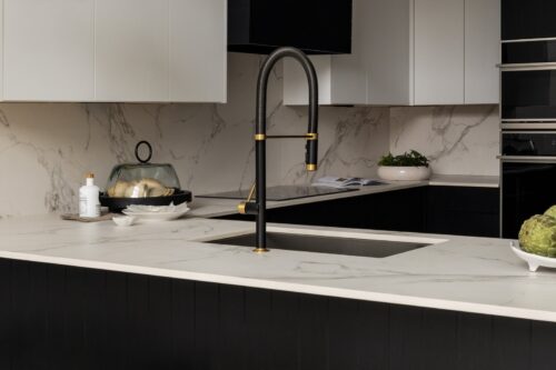Close-up of marble backsplash and black faucet with gold accents above custom kitchen cabinets Ludlow VT.