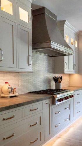 white kitchen cabinets with custom metal range hood and Wolf cooktop with stone countertops