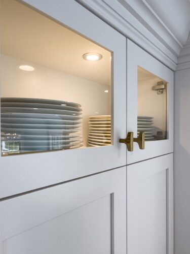 Glass-front cabinet with interior lighting and dishware storage in Nesconset NY custom kitchen.