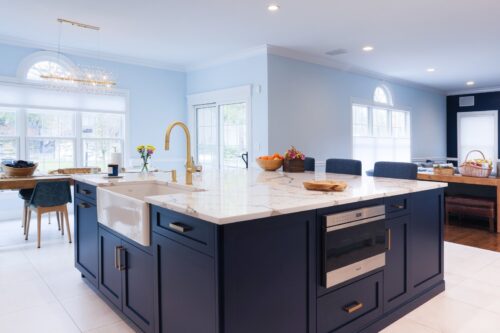 Kitchen island in Nesconset NY with farmhouse sink, gold faucet, navy cabinetry, and marble countertop.