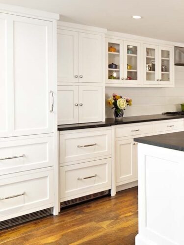 Close-up of glass-front cabinets and inset drawers in white shaker cabinetry with integrated refrigerator panels.