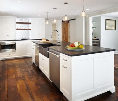 Kitchen island with farmhouse sink and two stainless dishwashers, pendant lighting, and walnut shelves in New Canaan home.