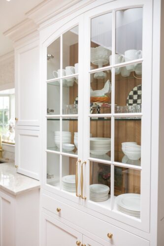 White kitchen remodel Cheshire CT with dual islands, custom cabinetry, and Taj Mahal quartzite for timeless style and function. Close up of glass paneled mullion cabinet with natural finished bead board interior.
