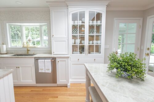 White kitchen remodel Cheshire CT with dual islands, custom cabinetry, and Taj Mahal quartzite for timeless style and function. Close up of glass paneled mullion cabinet with natural finished bead board interior.