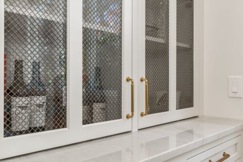 White built in cabinetry with glass paneled doors with a wire mess insert. Walnut cabinet interior.