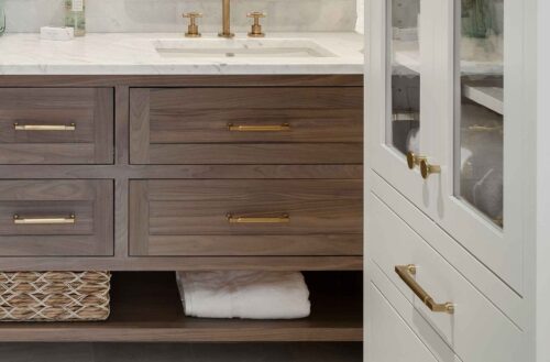 Close-up of walnut vanity drawers with brass hardware beside tall painted maple cabinet in an Exeter NH custom bathroom remodel.
