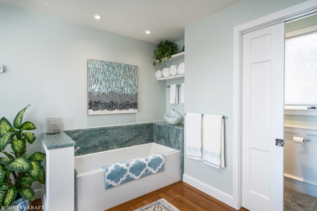 Master bath in Winchester, Massachusetts features a white bath tub with white open shelves and white trim and molding