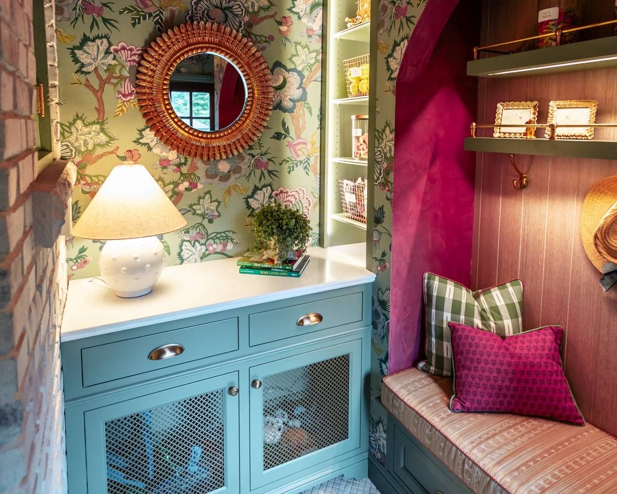 Wide angle view of the mudroom cabinetry, floral wallpaper, and round mirror in the Designer Show House kitchen.