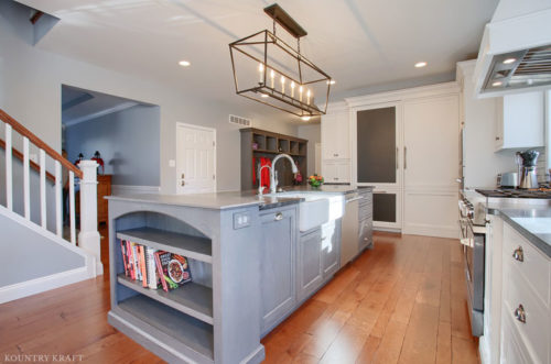 Custom Gray Wolf kitchen island cabinets with white farmhouse sink, stainless dishwasher and built-in bookshelf end