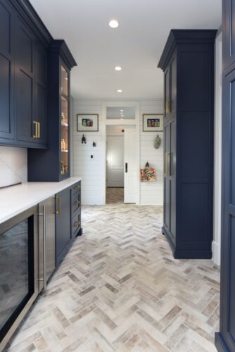 Butler’s pantry with dark blue cabinetry and matte brass hardware offering ample storage and a beverage center.