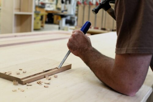 Skilled craftsman at Kountry Kraft Cabinet Makers hand chiseling wood, highlighting precision woodworking and custom cabinetry.