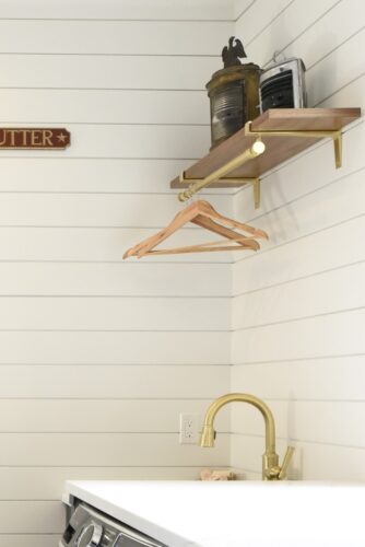 Laundry room remodel in Edgewater MD with custom Hale Navy cabinetry, brass accents, and shiplap walls. Focus is on the bright white shiplap walls, matte brass utility sink faucet and self with rod for hanging clothing for drying.