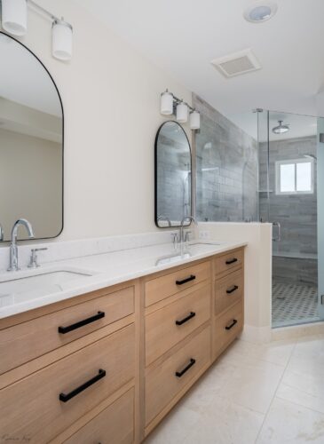 Double vanity with rift cut white oak cabinetry, quartz countertop, and arched mirrors in a Sea Isle City master bath remodel.