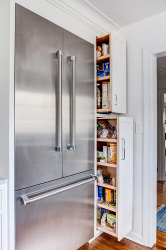 Small kitchen cabinetry. Finished in a white paint framing a stainless steel refrigerator. Vertical pull out down right side of refrigerator.