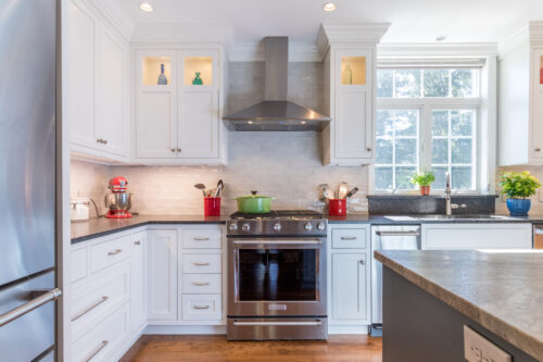 Small kitchen cabinetry. White painted kitchen cabinetry with glass doors on wall cabinets. Light backsplash and dark countertops.