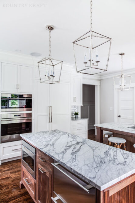 Custom cabinetry crafted for a white transitional kitchen has an integrated refrigerator and marble countertops