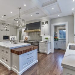 Custom kitchen with White Dove cabinetry, oversized island, butcher block detail, and black-and-brass range hood.