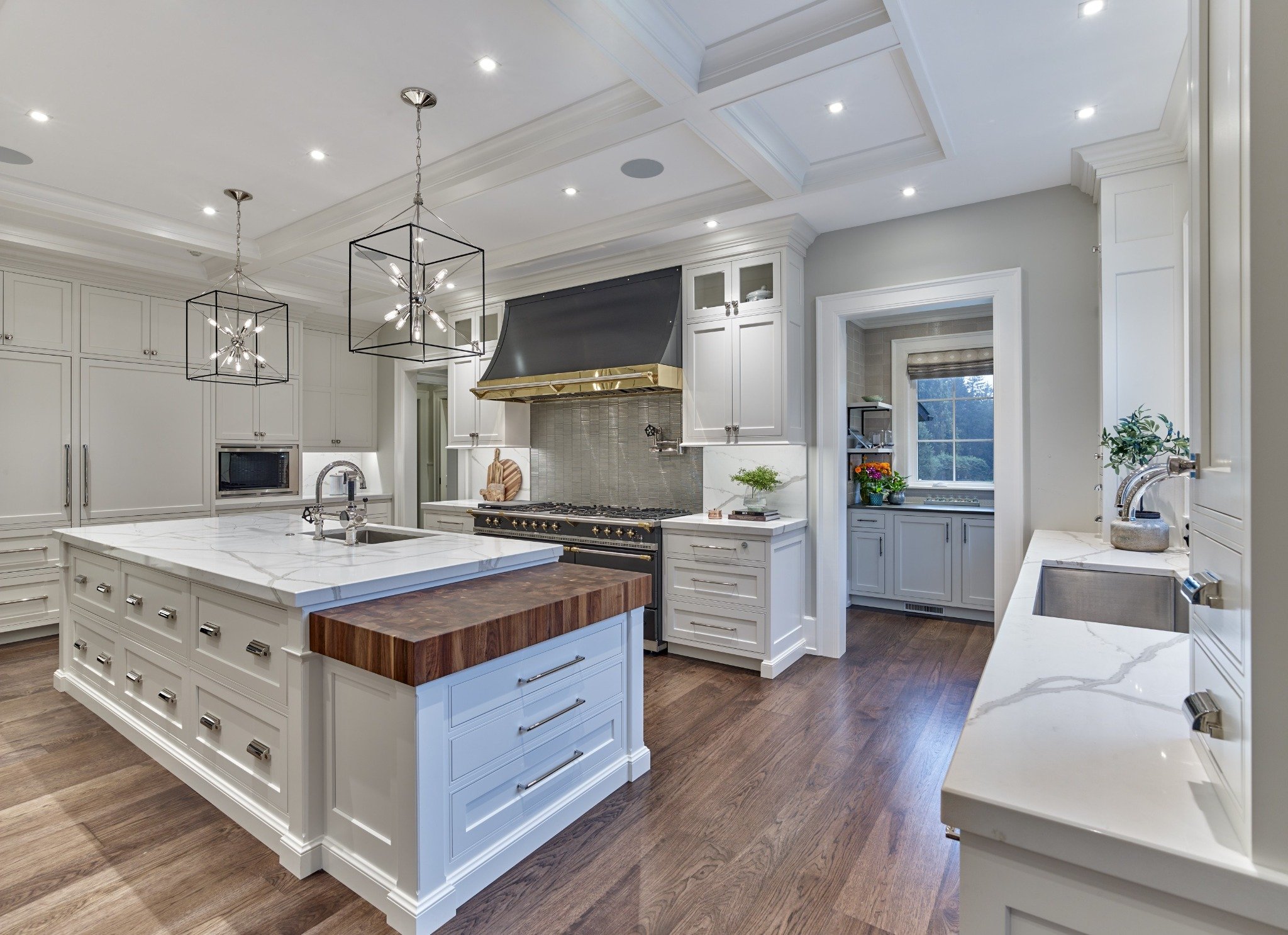 Custom kitchen with White Dove cabinetry, oversized island, butcher block detail, and black-and-brass range hood.