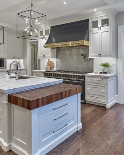 Focus on the range wall in custom Villanova kitchen featuring black-and-brass hood, inset cabinetry, and veined stone backsplash.