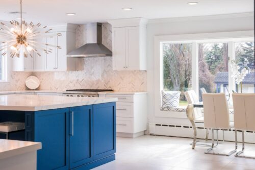 Close view of blue kitchen island with white marble countertop and starburst chandelier in Brookville NY remodel.