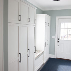White entryway cabinets provide storage and include a window bench for seating in Madison, NJ