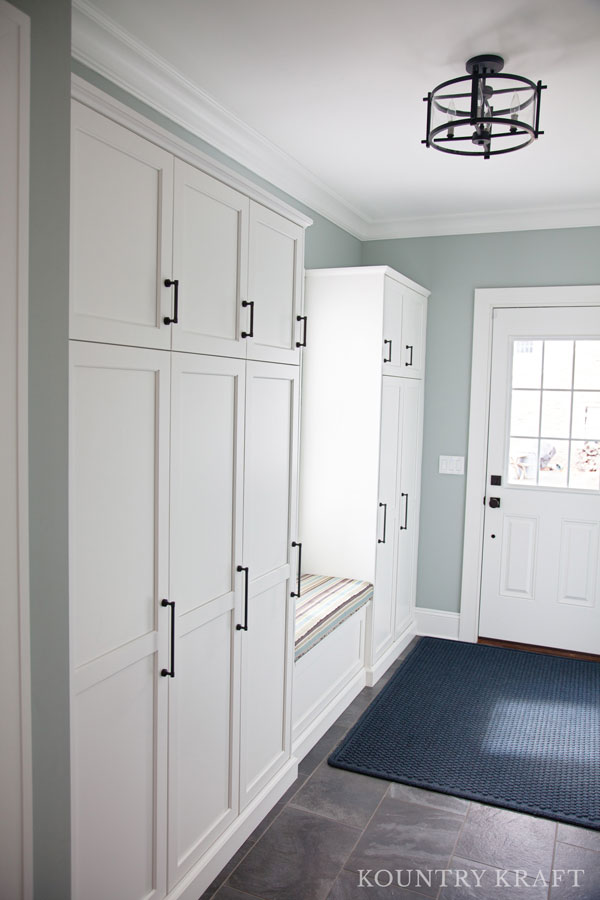 White entryway cabinets provide storage and include a window bench for seating in Madison, NJ